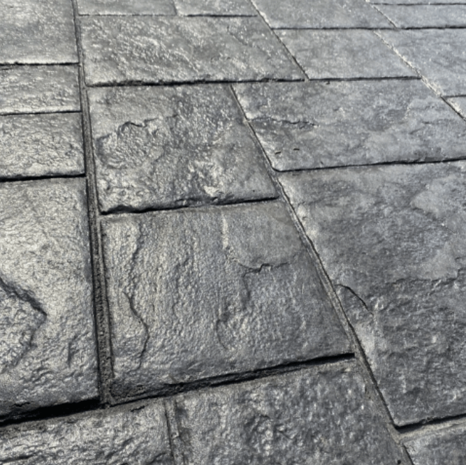 A close-up view of dark grey, textured stone pavers stamped concrete driveway arranged in a rectangular grid pattern.