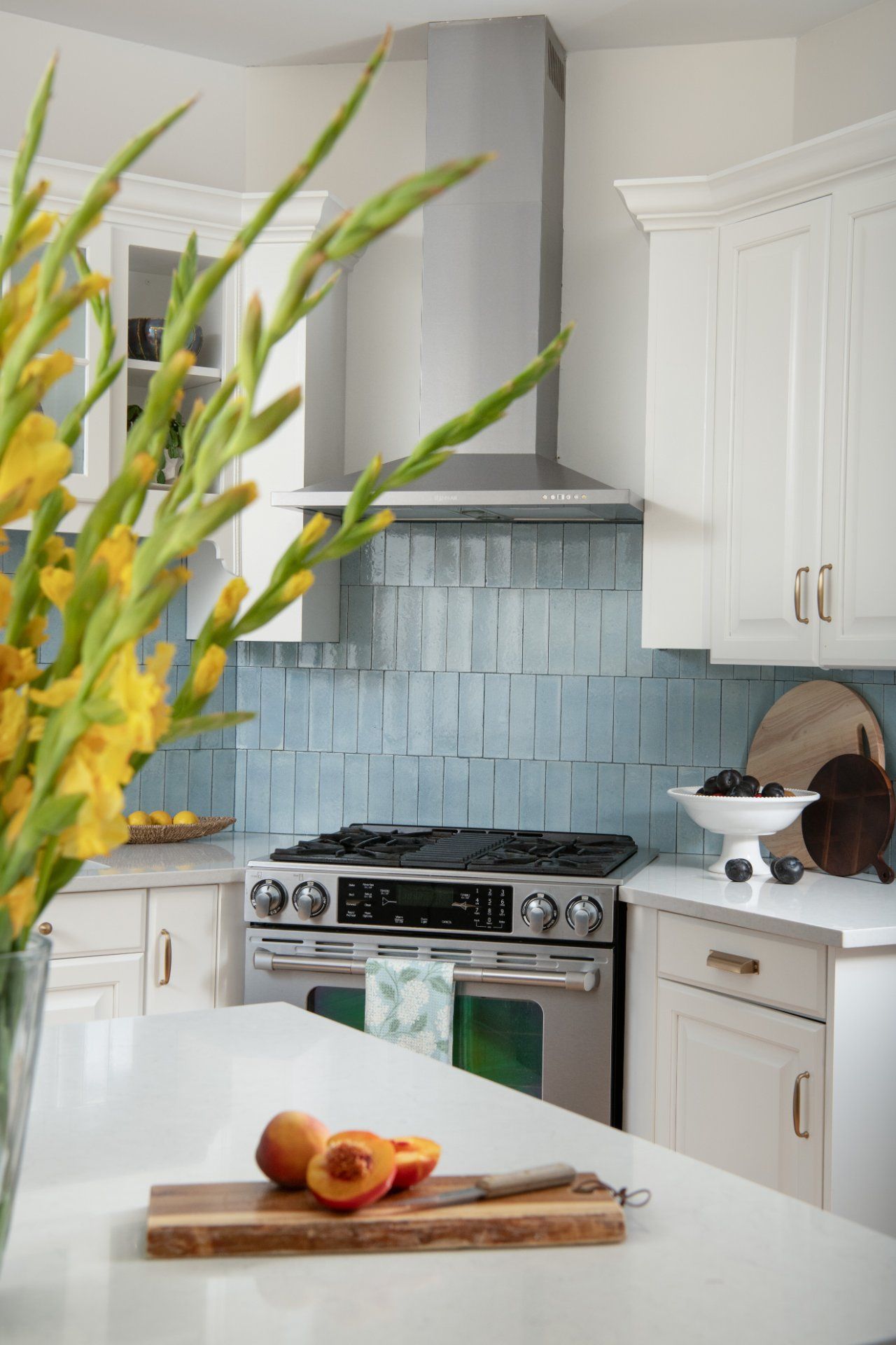Kitchen interior with light blue backsplash, stainless steel appliances, and white cabinets. Yellow flowers and cut peaches in foreground | Charlotte, NC | An Inspiring Home