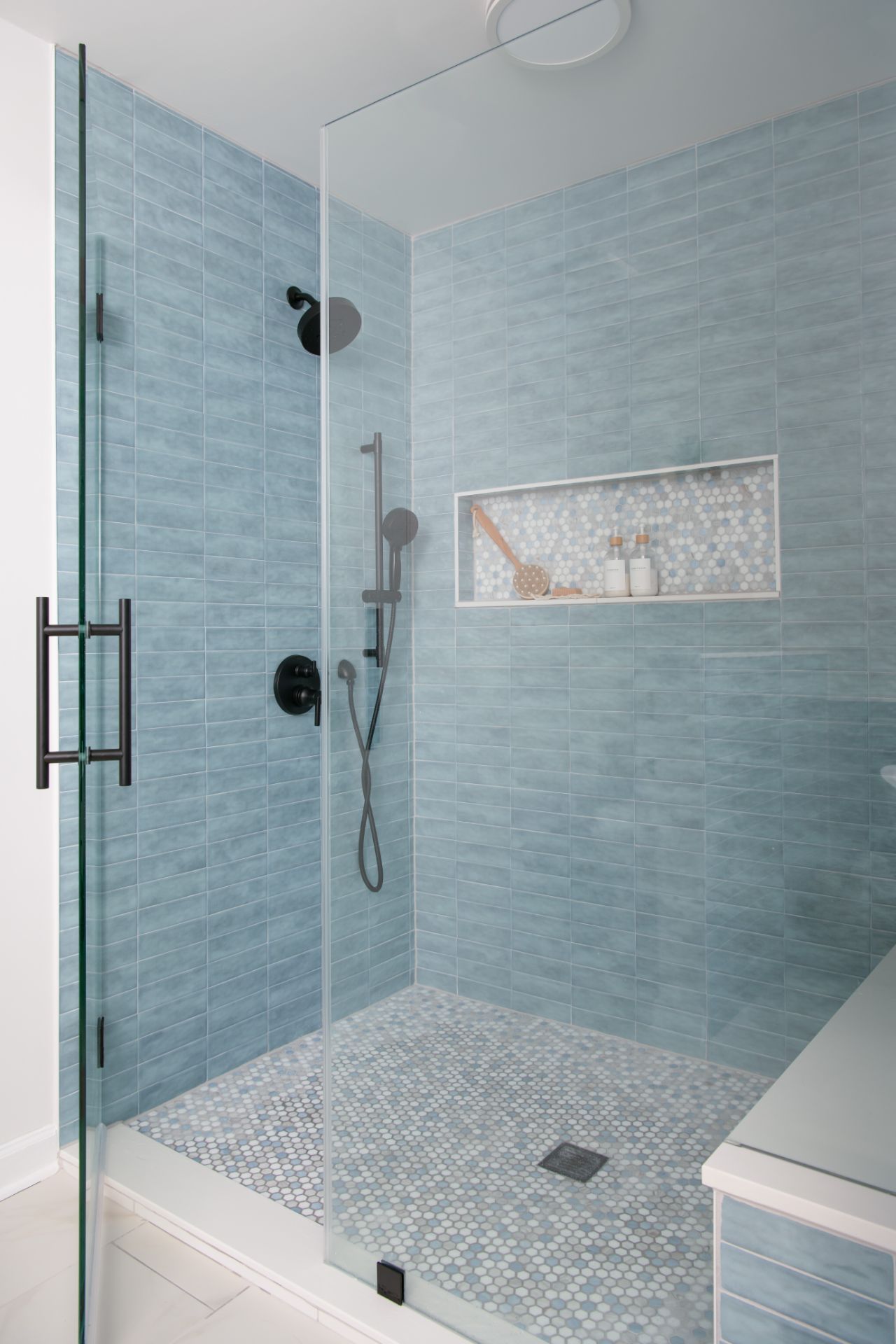 Blue-tiled shower with glass door and black fixtures. Built-in shelf, light-blue floor, and white trim | Charlotte, NC | An Inspiring Home