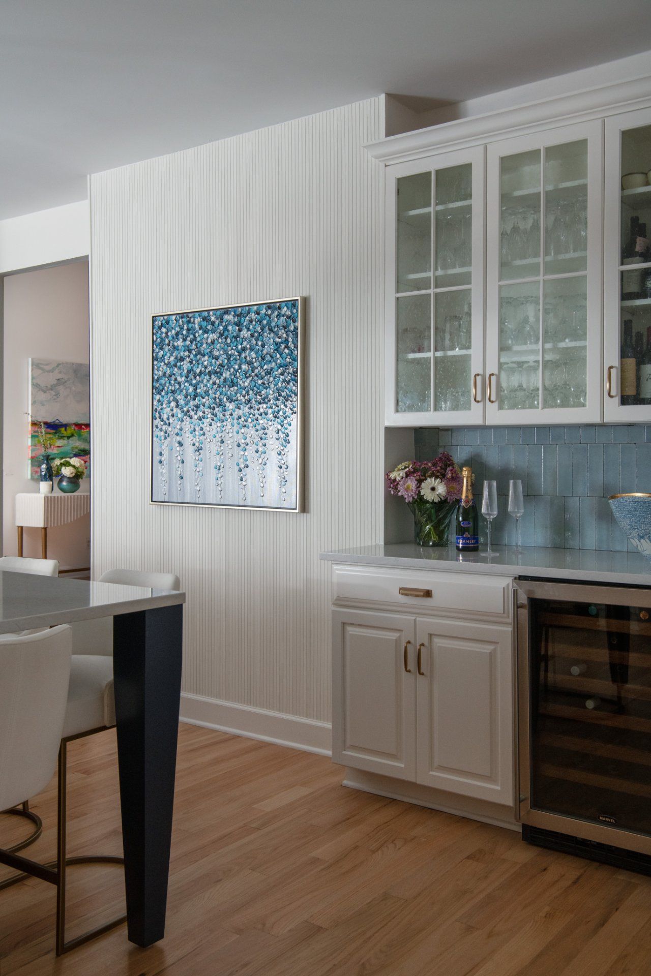 Kitchen with white cabinets, wine cooler, blue backsplash, artwork, and light wood flooring | Charlotte, NC | An Inspiring Home