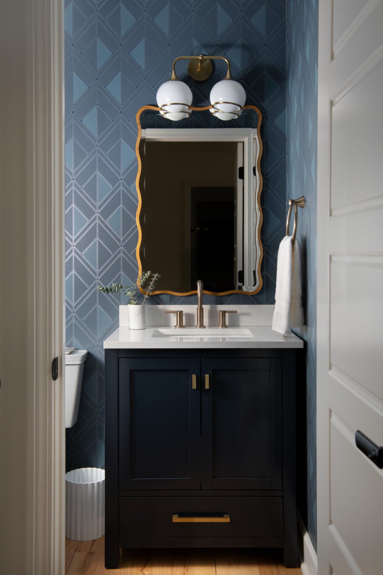 Small bathroom with navy vanity, gold mirror and lighting, blue patterned wallpaper | Charlotte, NC | An Inspiring Home