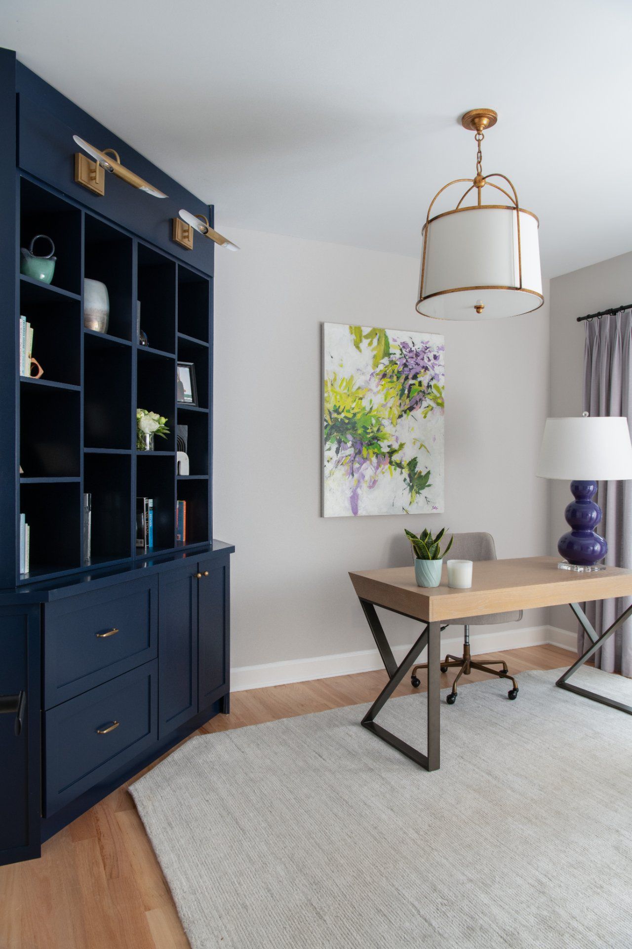 Navy blue built-in shelving and desk in a home office. Light gray walls, light wood floor, rug, art, and a gold and white light fixture | Charlotte, NC | An Inspiring Home