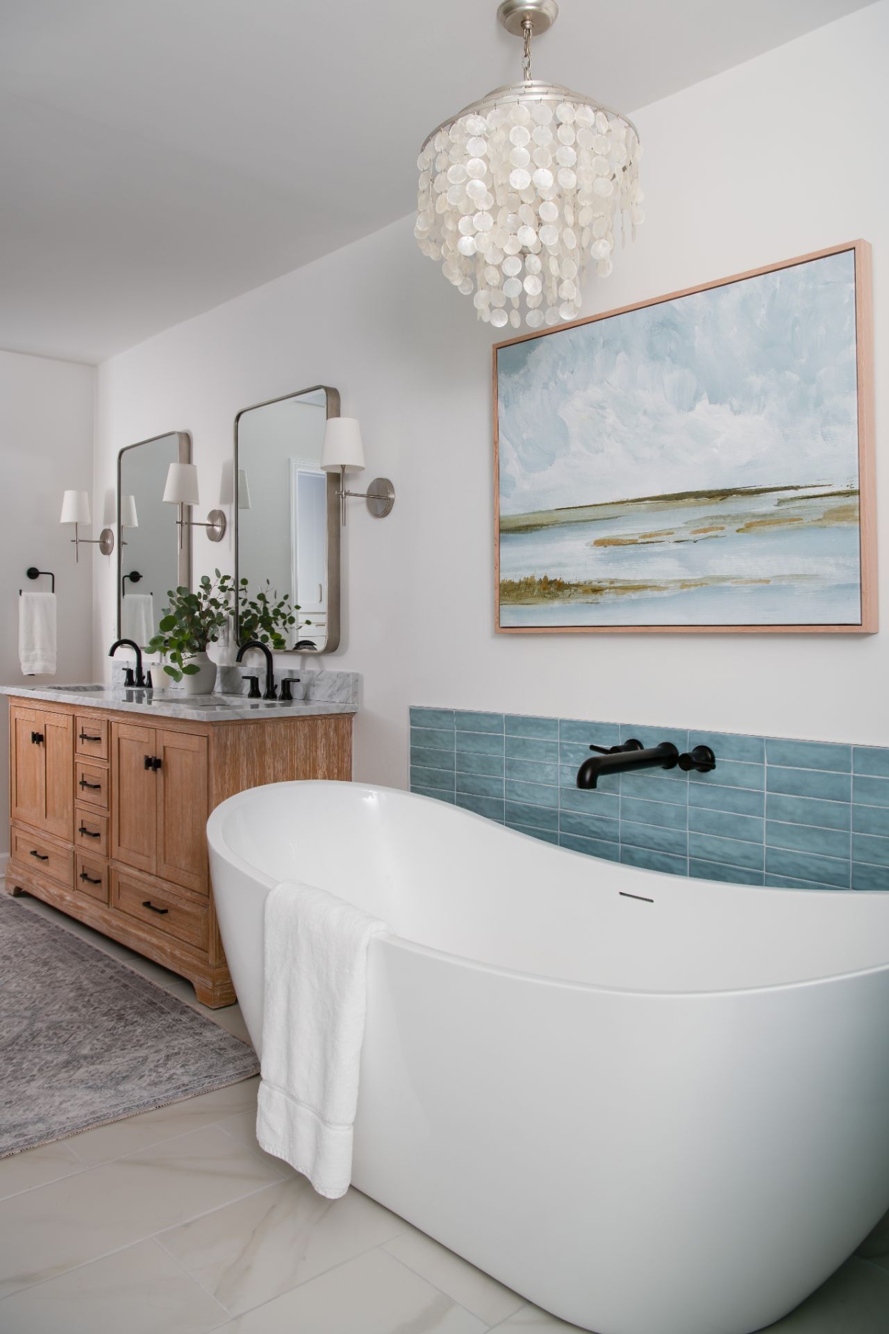 Bathroom with a white soaking tub, double vanity, blue tile accent, and artwork, lit by a chandelier | Charlotte, NC | An Inspiring Home