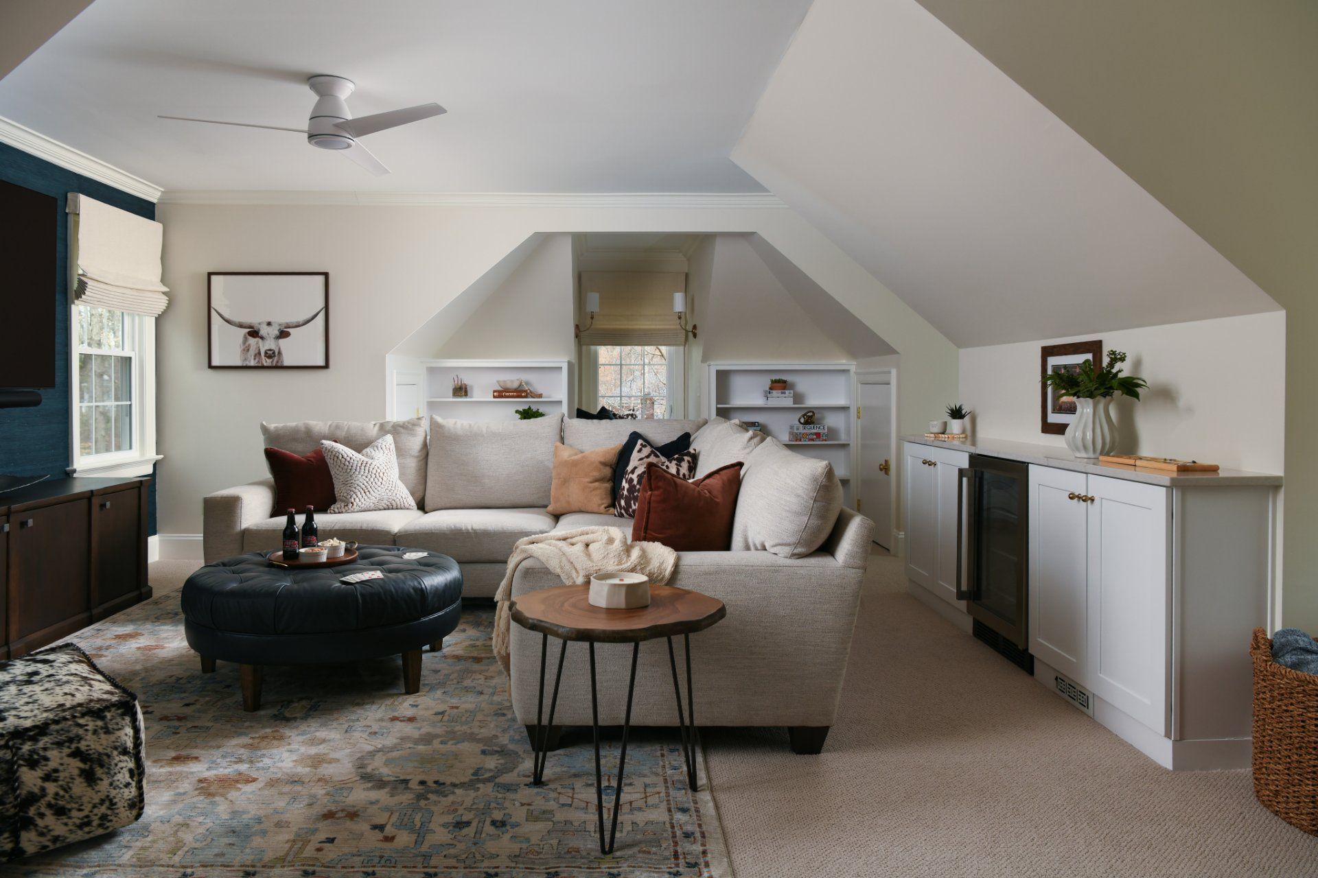 Bright living room with beige sofa, dark ottoman, patterned rug, and built-in cabinets under a sloped ceiling | Weddington, NC | An Inspiring Home