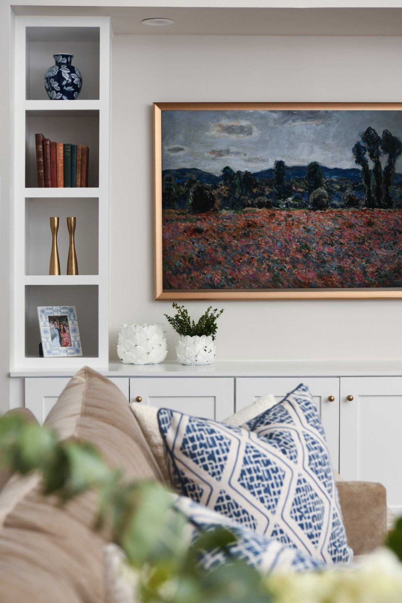 Bright living room with framed landscape art, white shelving, and blue-and-white patterned pillows | Weddington, NC | An Inspiring Home