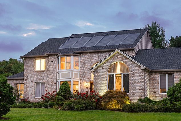 Photo of two story house at dusk with lights on inside, and solar shingles on top of house