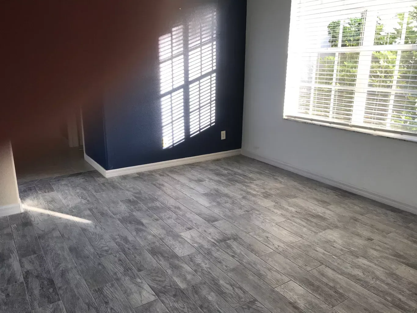 A room with hardwood floors and a window with blinds.