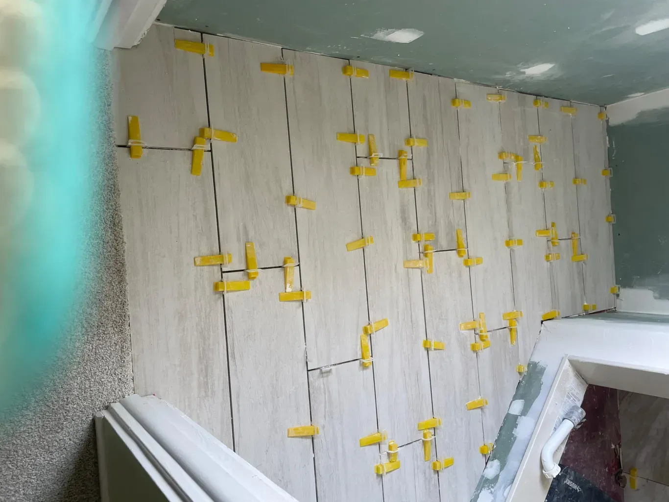A tile wall is being installed in a bathroom with yellow clips.