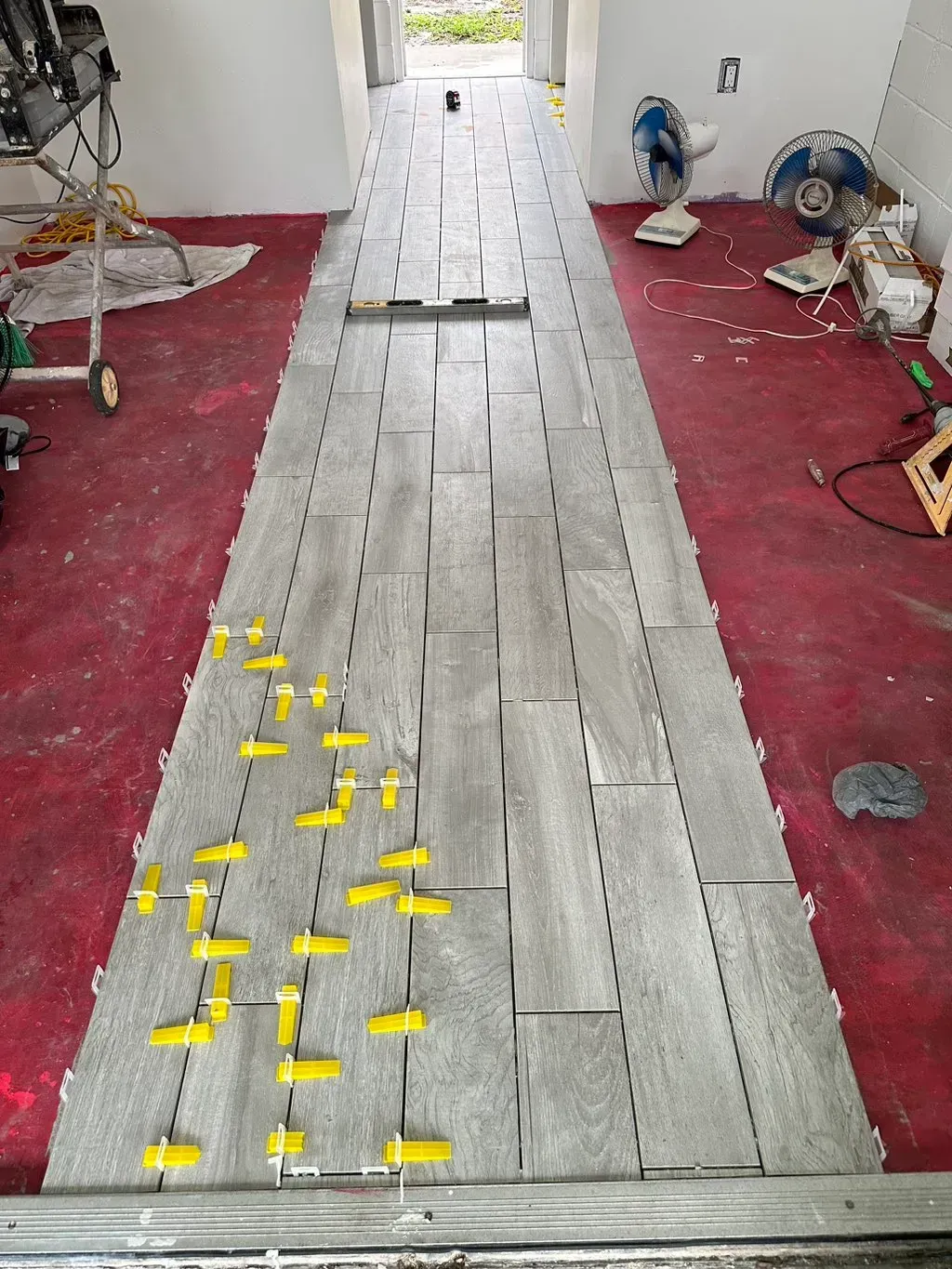 A long hallway with tiles being installed on the floor.