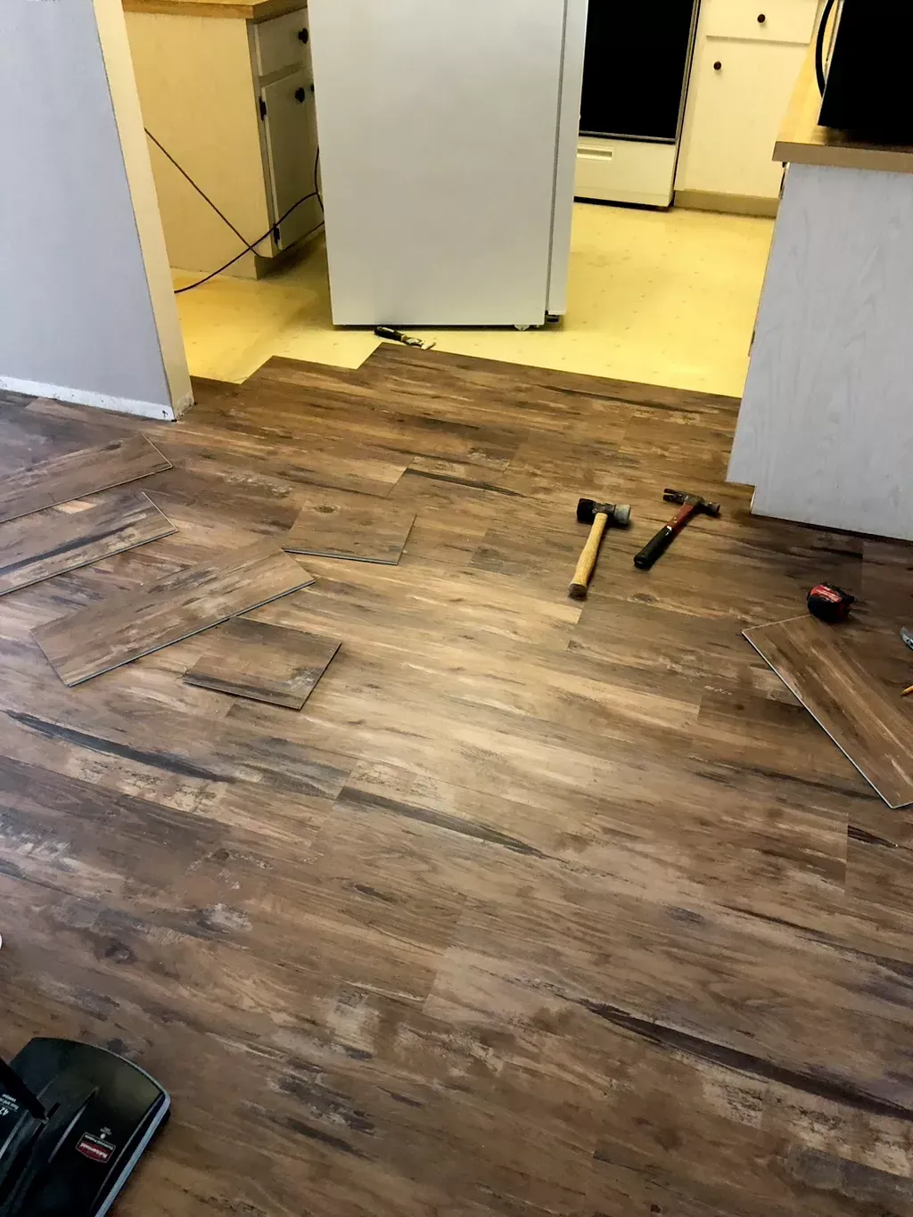 A kitchen with a wooden floor and a vacuum cleaner on the floor.
