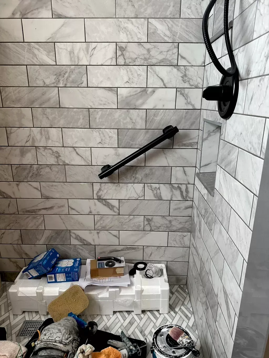 A bathroom with marble tiles and a black handle on the shower head.
