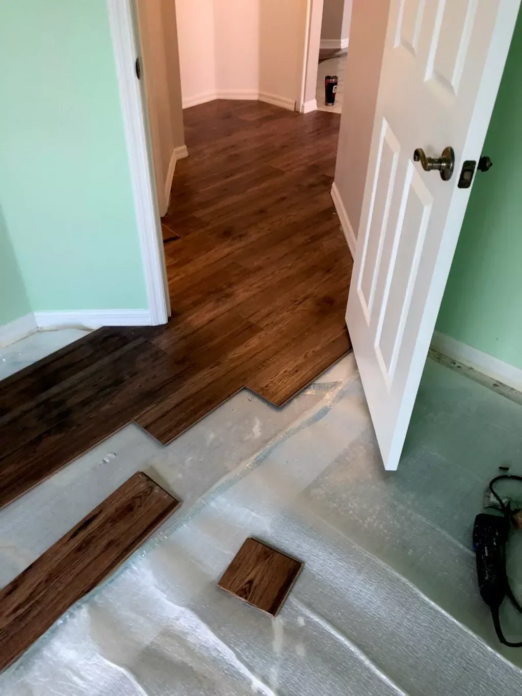A wooden floor is being installed in a room with a door open.
