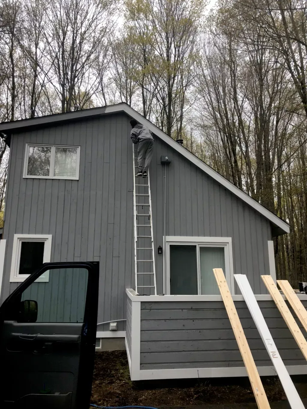 A man is standing on a ladder on the side of a house.