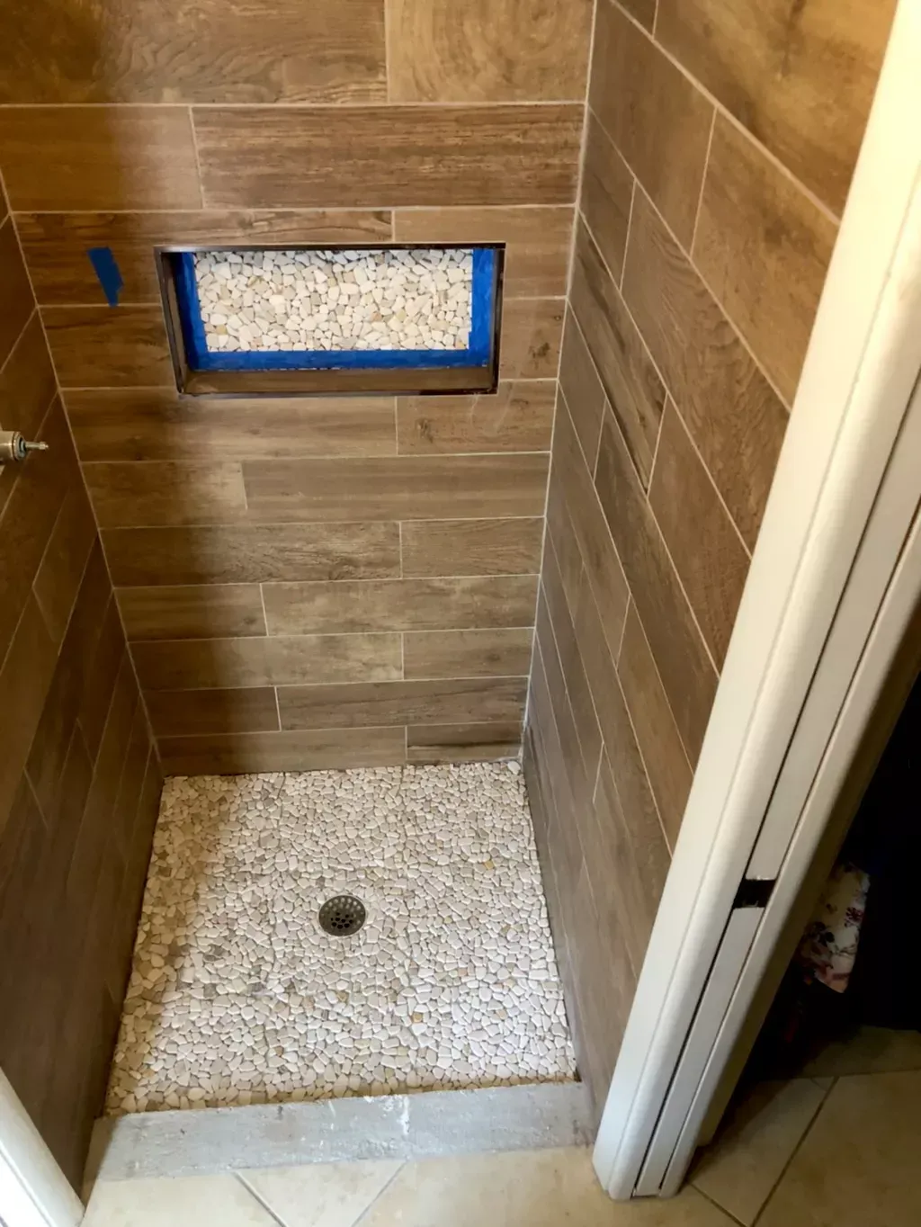 A shower stall with wooden tiles and gravel in a bathroom.