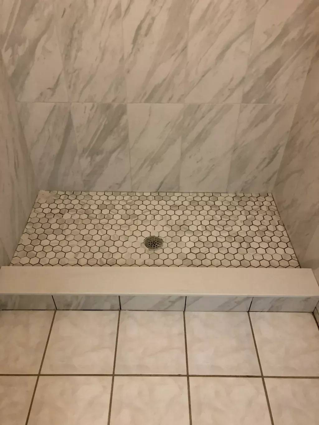 A shower stall with white tiles and marble walls