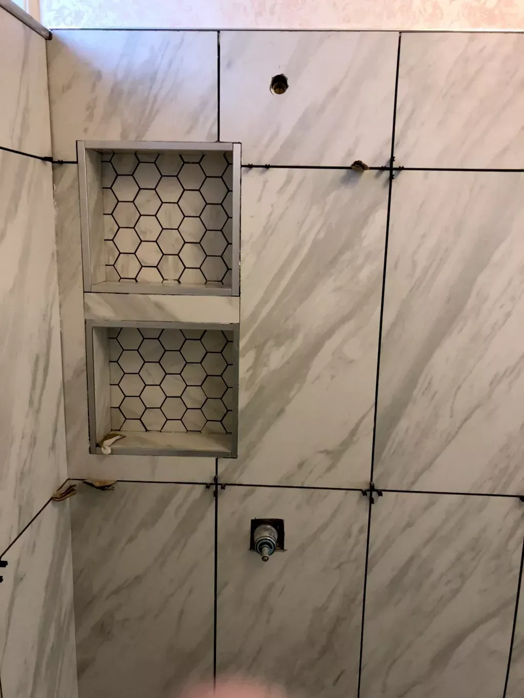 A bathroom with marble tiles and a honeycomb shower niche.