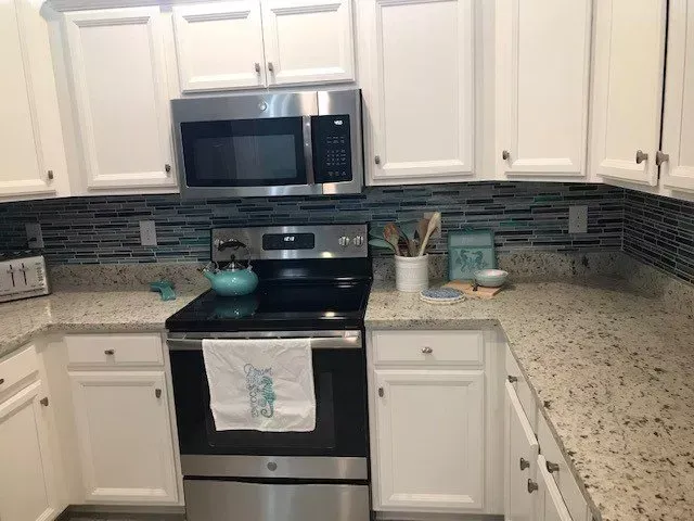 A kitchen with white cabinets , stainless steel appliances , and granite counter tops.