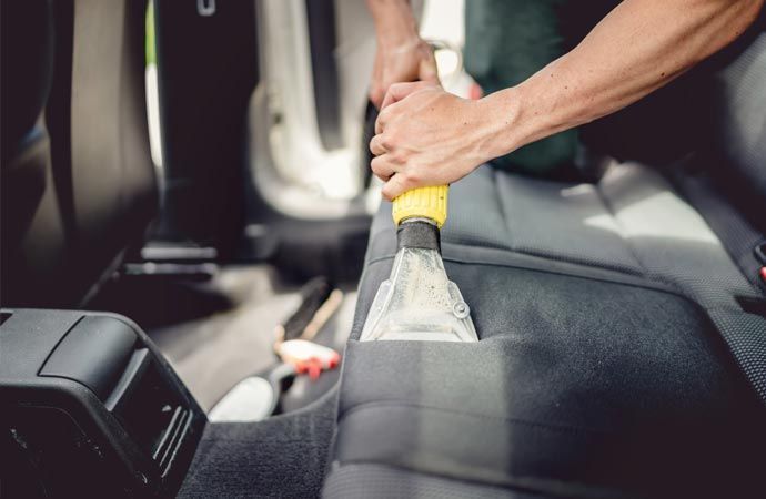 A person is cleaning the back seat of a car with a vacuum cleaner.