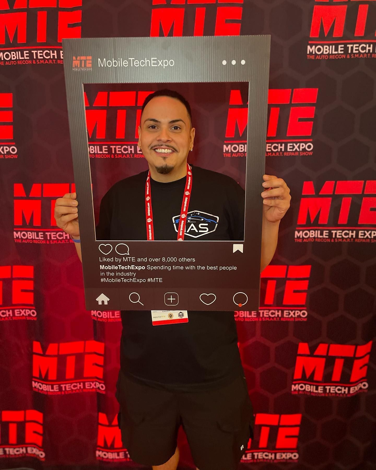 A man is holding a picture frame in front of a wall that says mobile tech expo