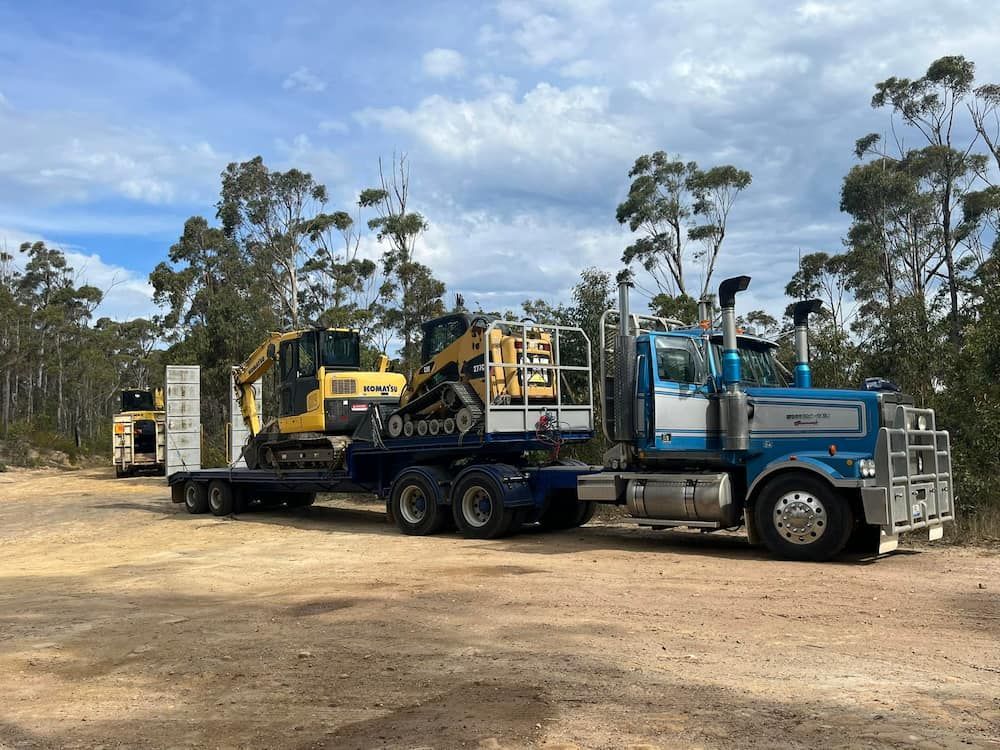 A Blue Semi Truck is Carrying a Yellow Excavator on a Trailer — BeCivil in Nowra, NSW