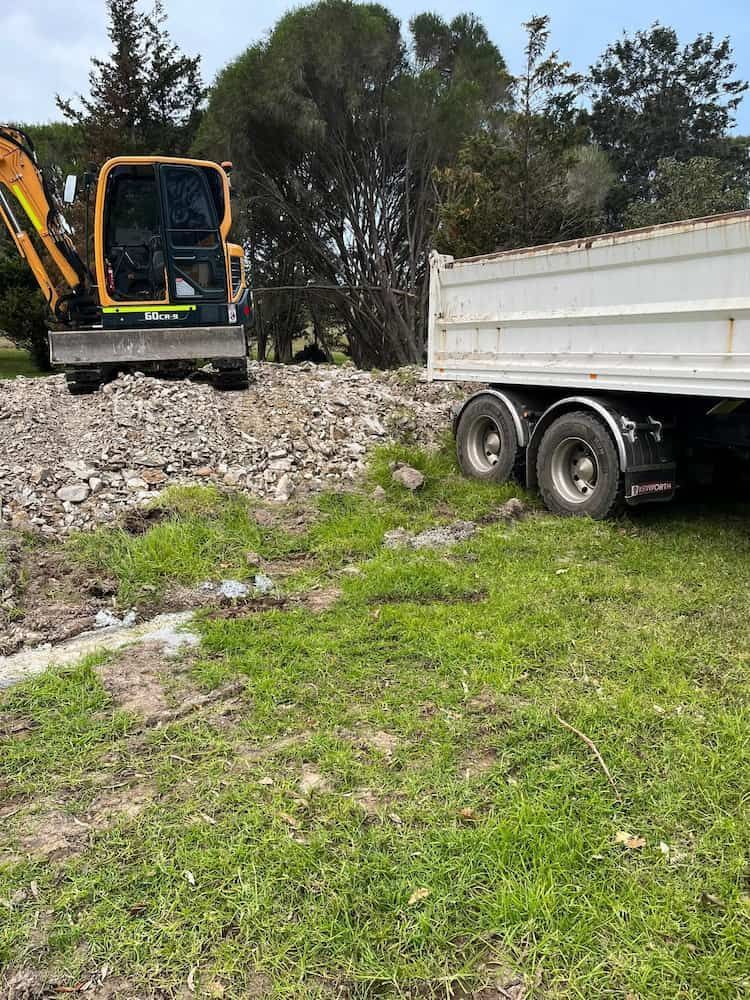 An Excavator is Sitting on Top of a Pile of Rocks Next to a Dump Truck — BeCivil in Jervis Bay, NSW