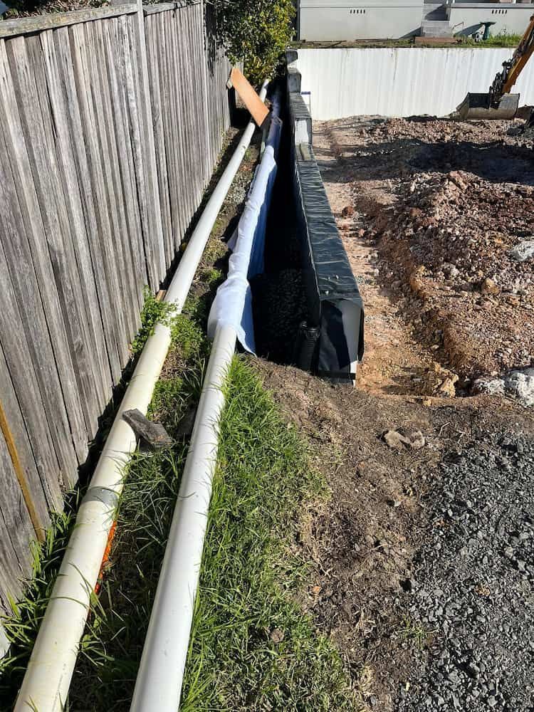 A Drainage System is Being Installed Next to a Wooden Fence 
