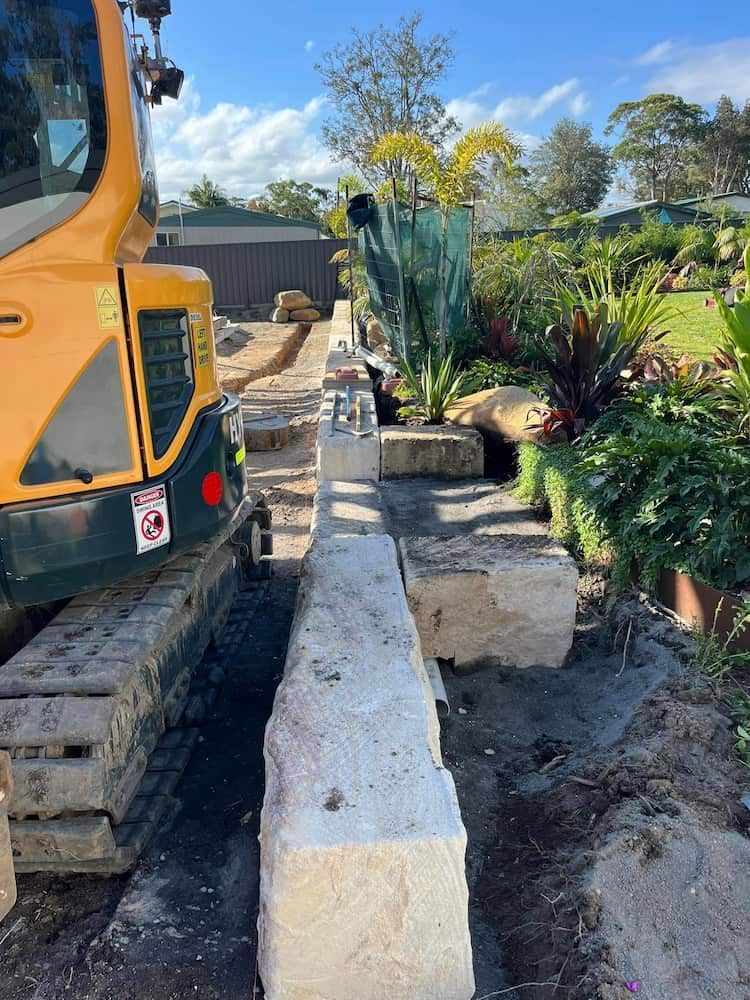 A Yellow Excavator is Moving a Large Stone Block in a Garden — BeCivil in Vicentia, NSW