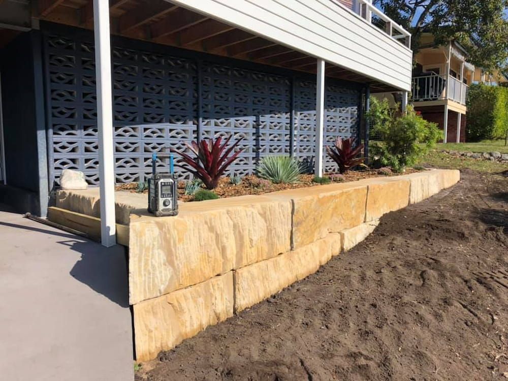 A Stone Wall With Plants Growing on It in Front of a House — BeCivil in Bomaderry, NSW