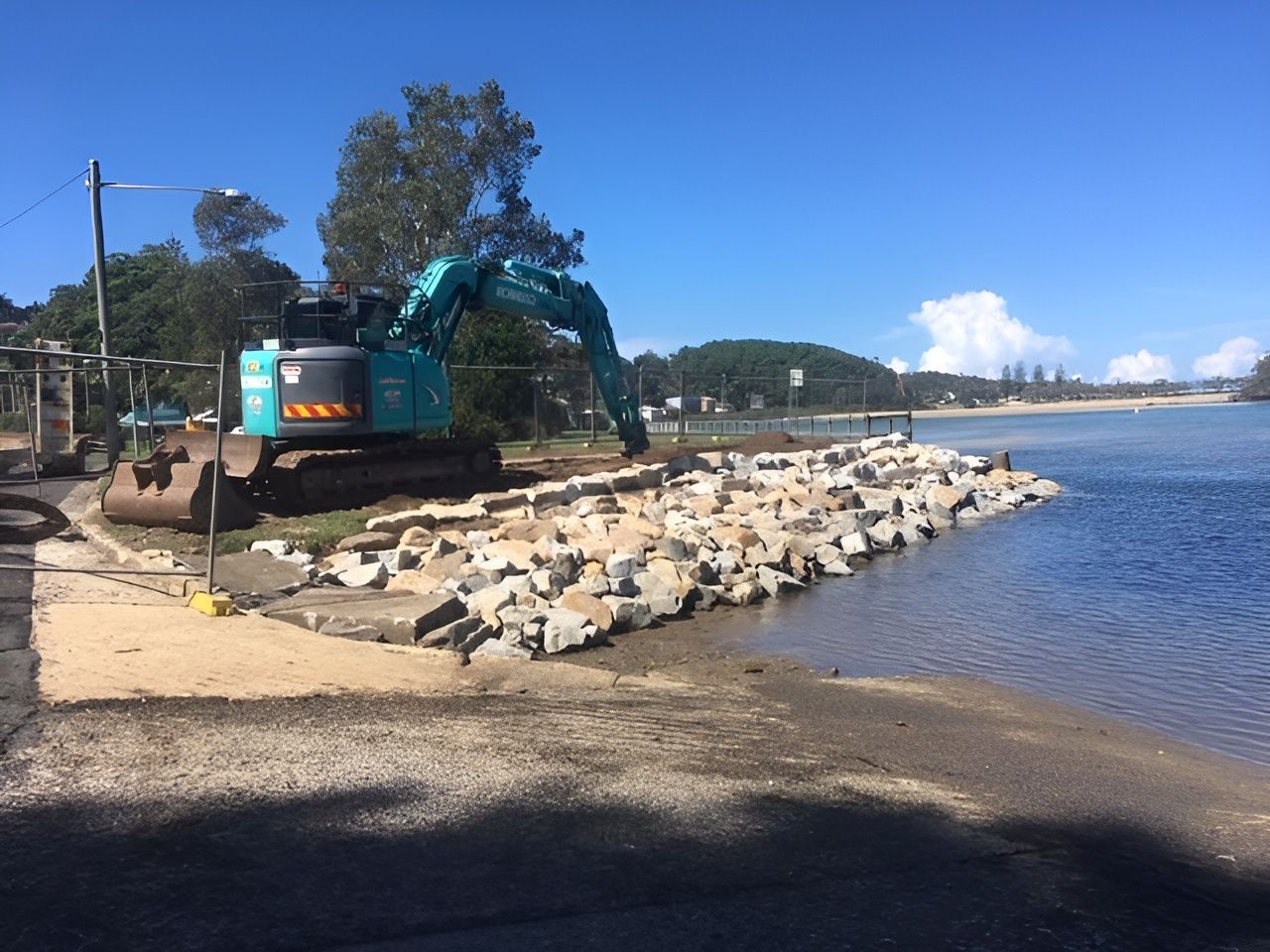 A Large Excavator Is Working On A Beach Next To A Body Of Water — Blue Dog Landscape Supplies In Newee Creek, NSW