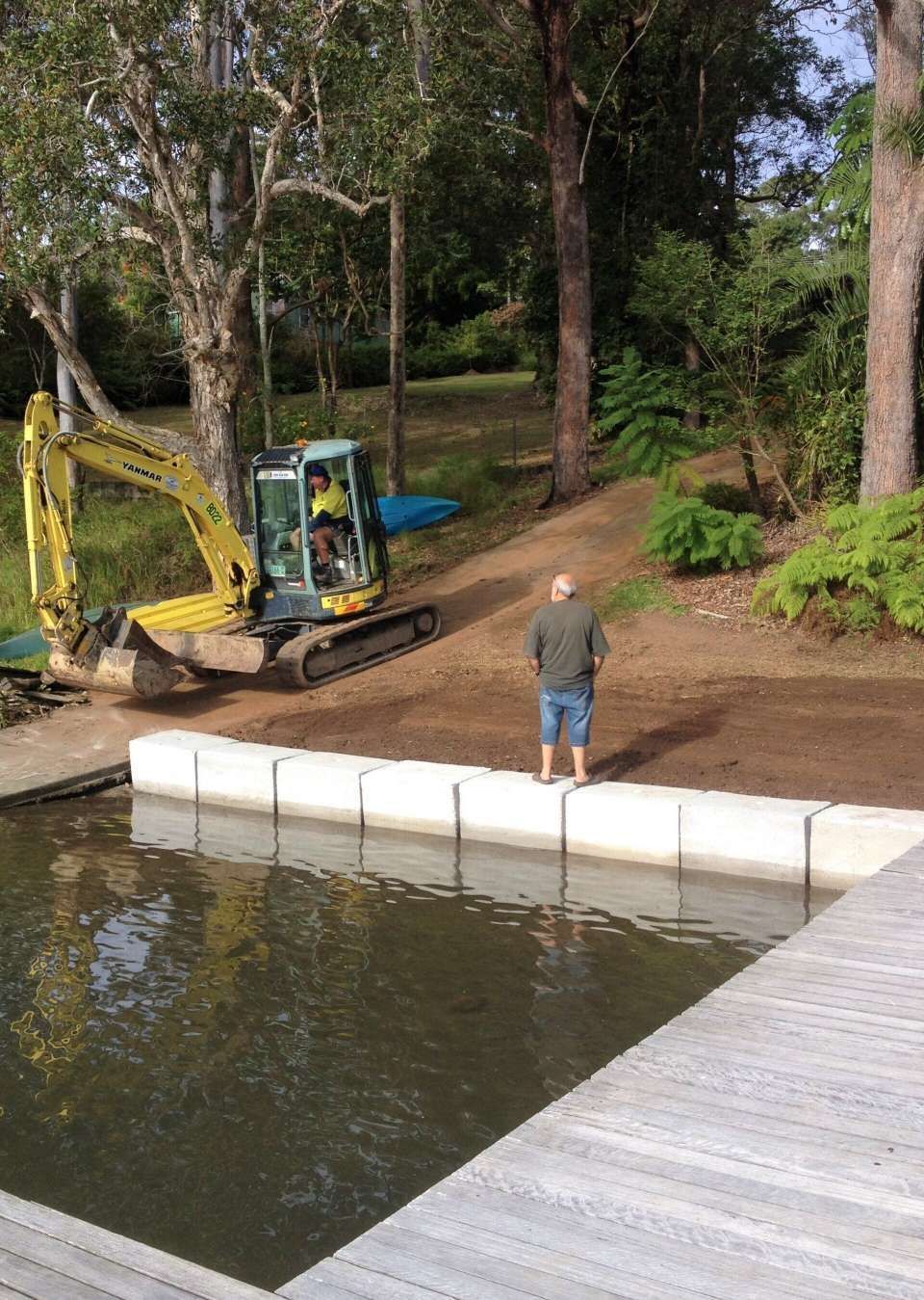 A Man Is Standing On A Dock Next To A Large Body Of Water — Blue Dog Landscape Supplies In Newee Creek, NSW