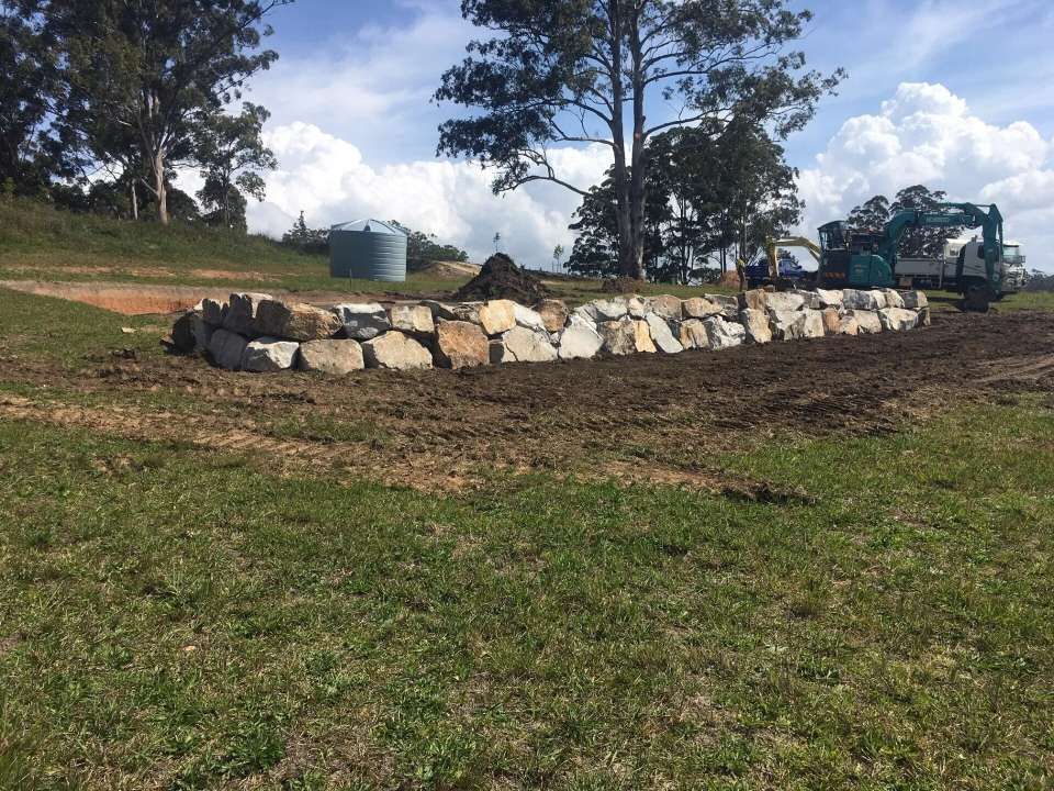 A Large Rock Wall Is Being Built In A Grassy Field — Blue Dog Landscape Supplies In Newee Creek, NSW