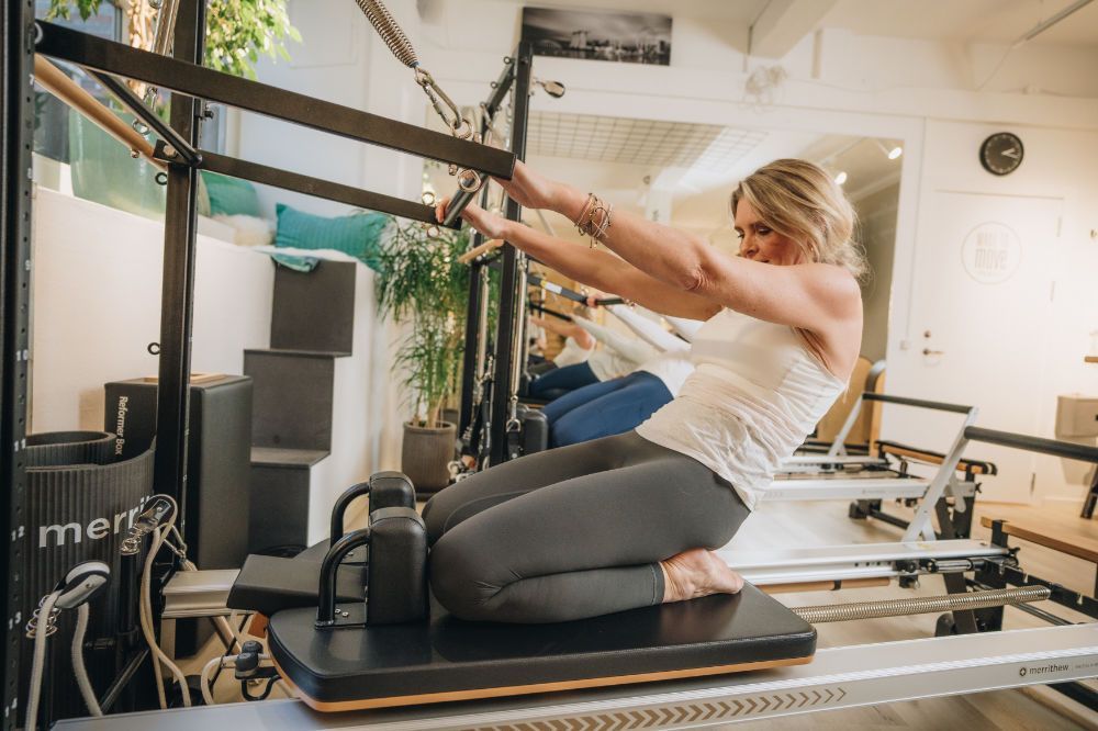 A woman is helping a man stretch his leg on a pilates cadillac