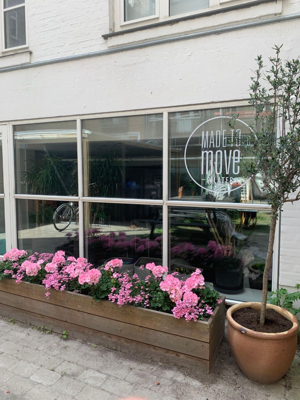 A wooden box filled with pink flowers is in front of a building.