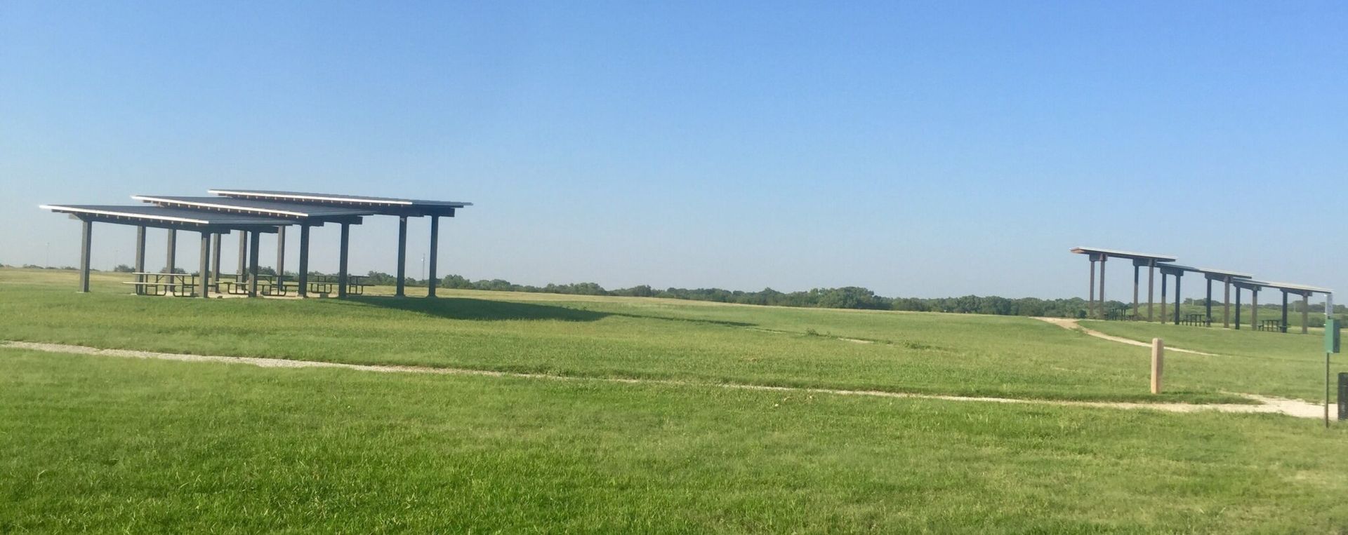 A row of wooden pergolas are sitting in the middle of a grassy field.