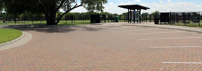 A brick walkway leading to a parking lot in a park.
