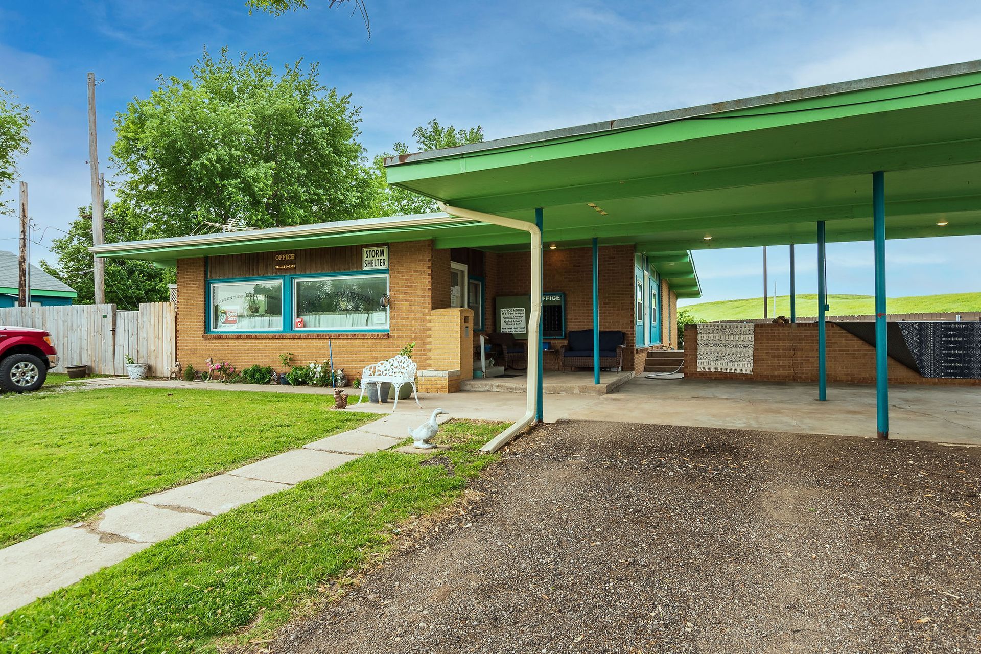A red truck is parked in front of a brick house with a green roof.