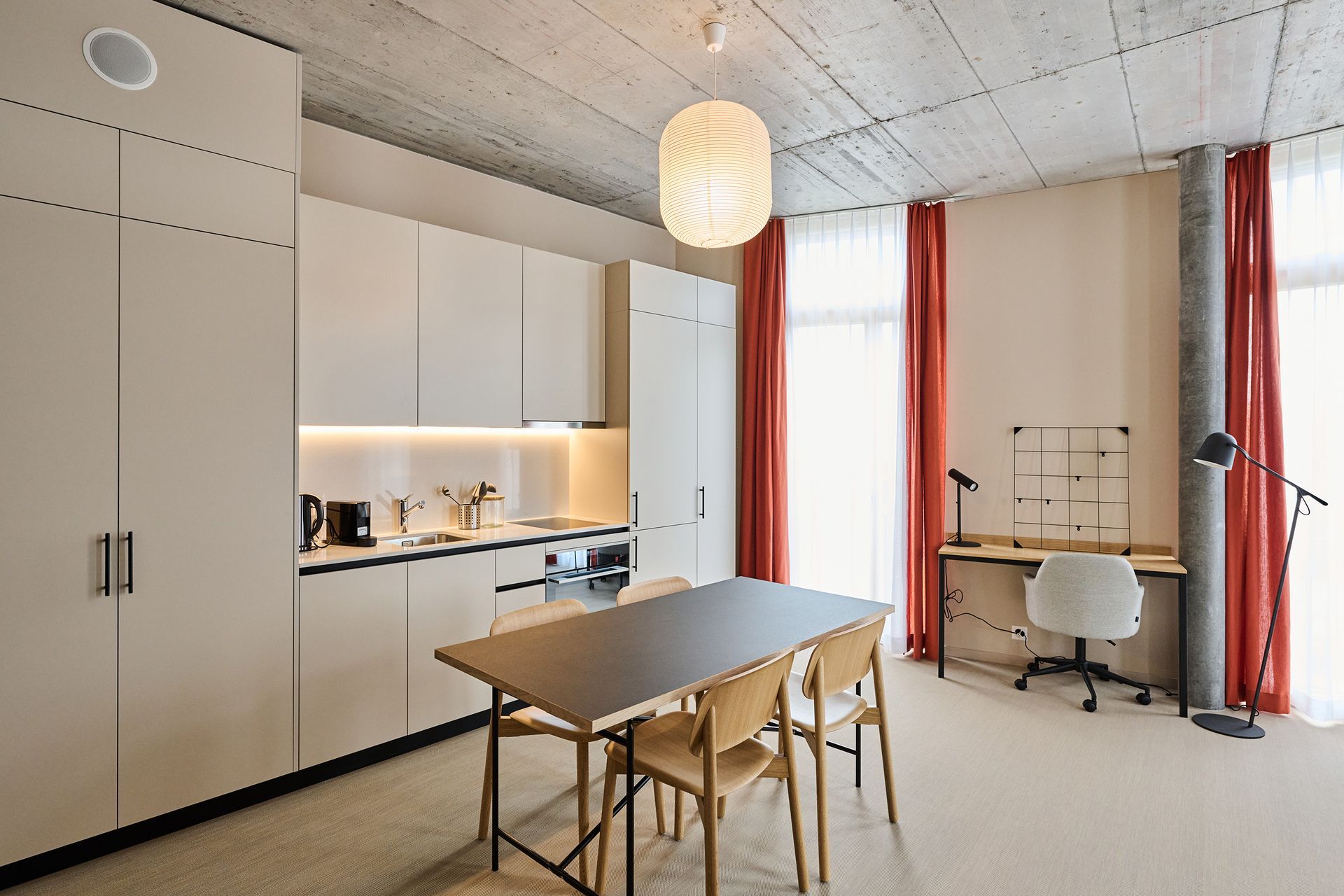 Bright modern kitchen-dining room with white cabinets, wooden table, and red curtains by tall windows