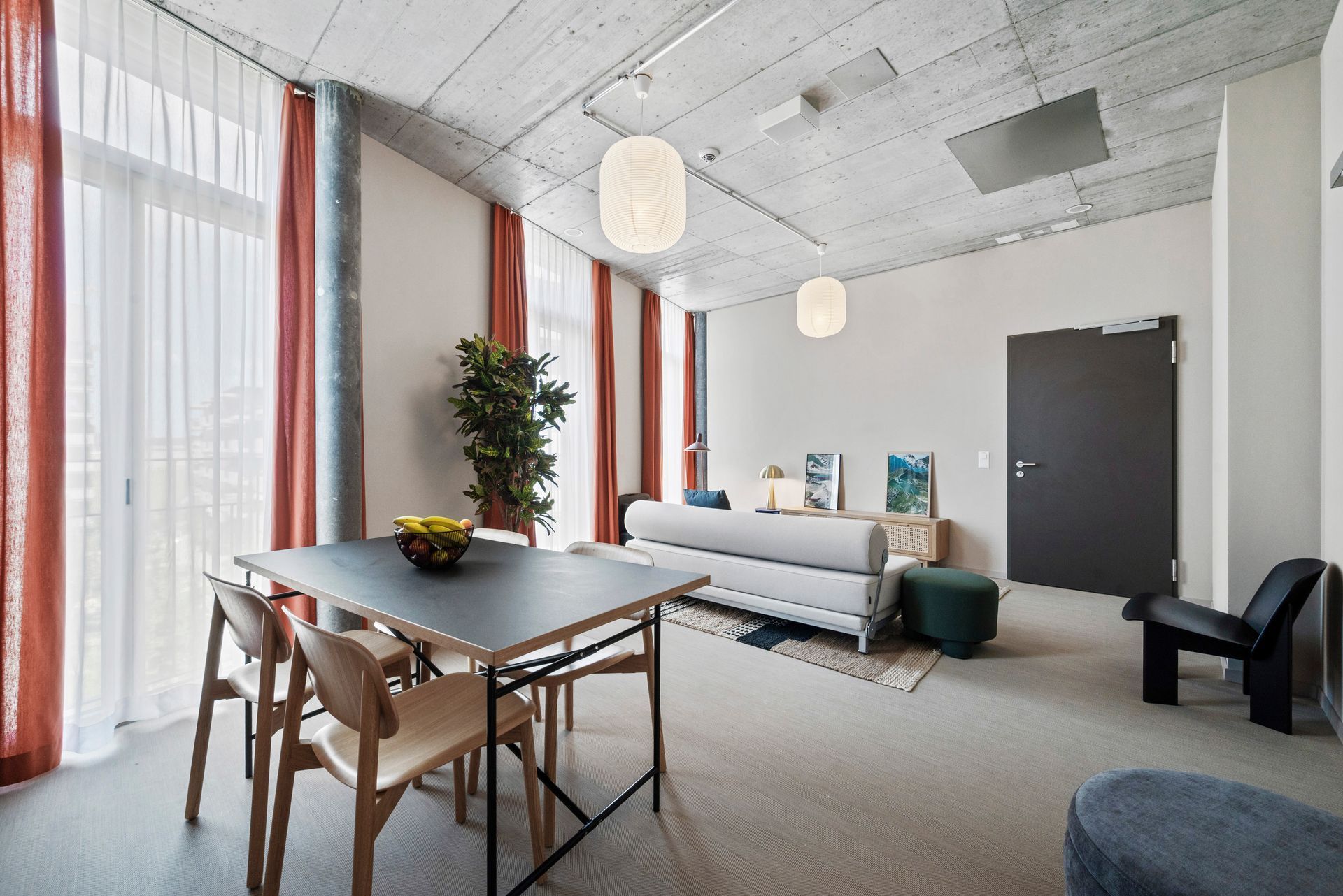 Bright modern living room with a sofa, dining table, large windows, and hanging pendant lights