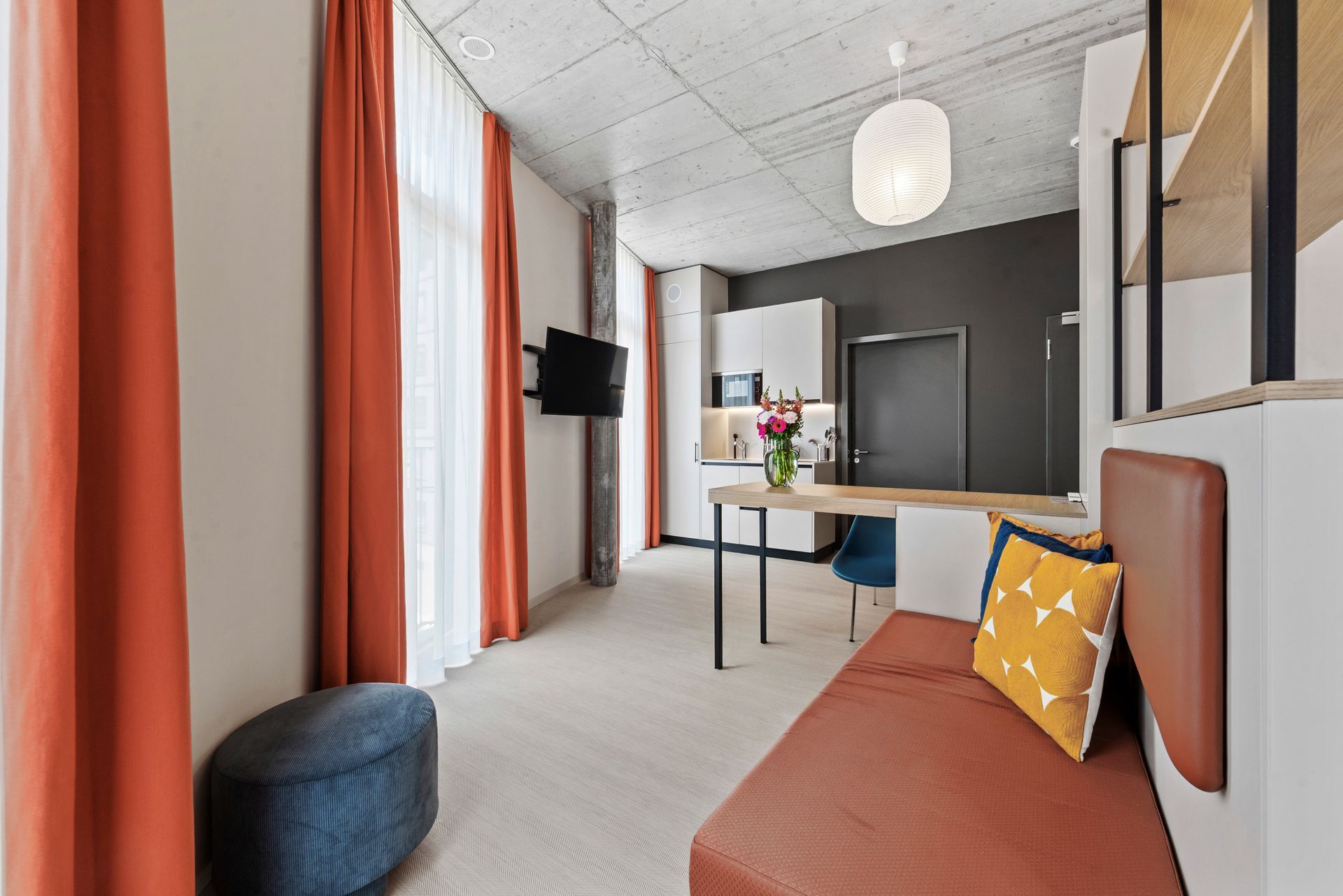 Modern living room with orange sofa, striped curtains, wall TV, and open kitchen view