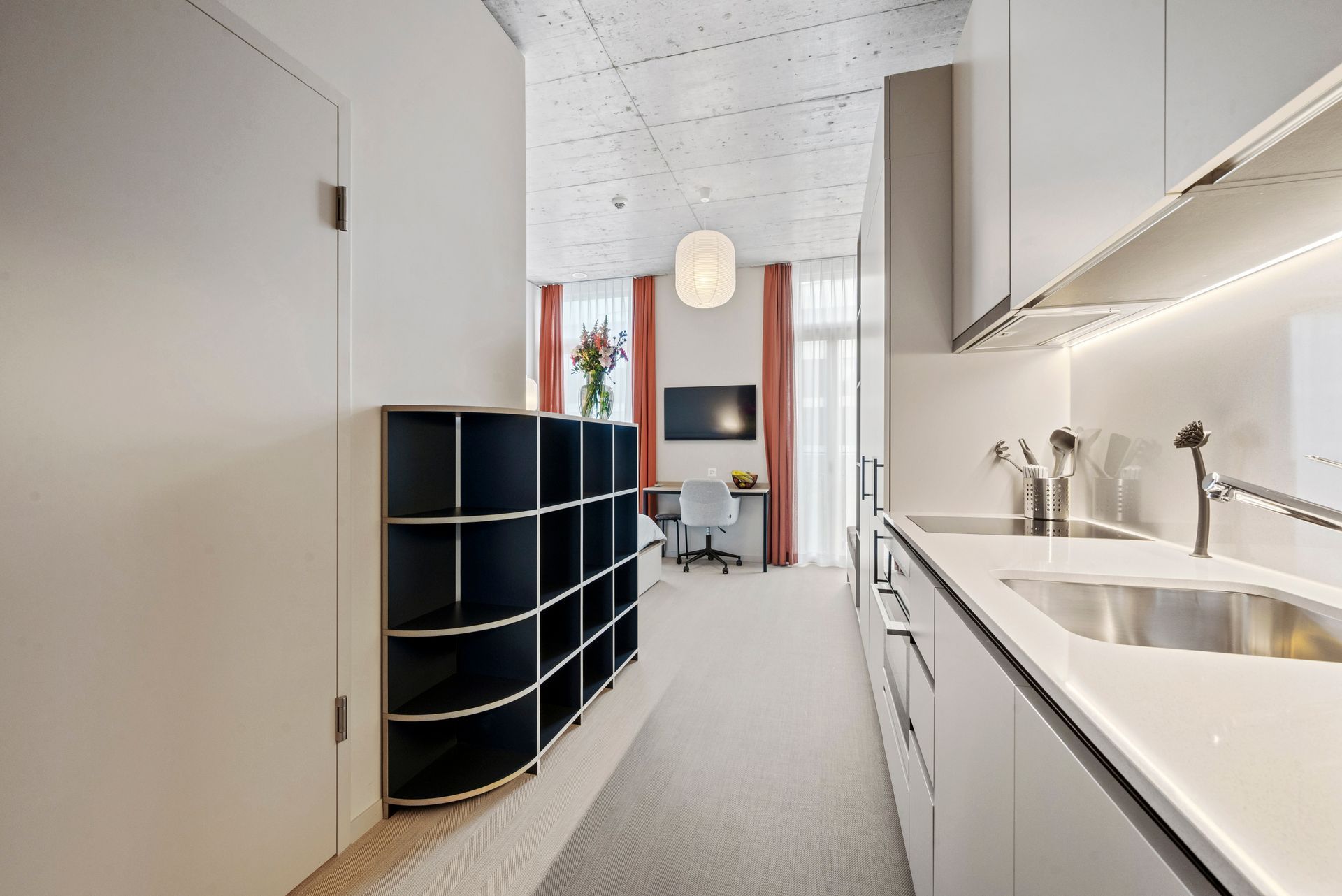 Modern kitchen with white cabinets, black shelving, and a view into a bright living area