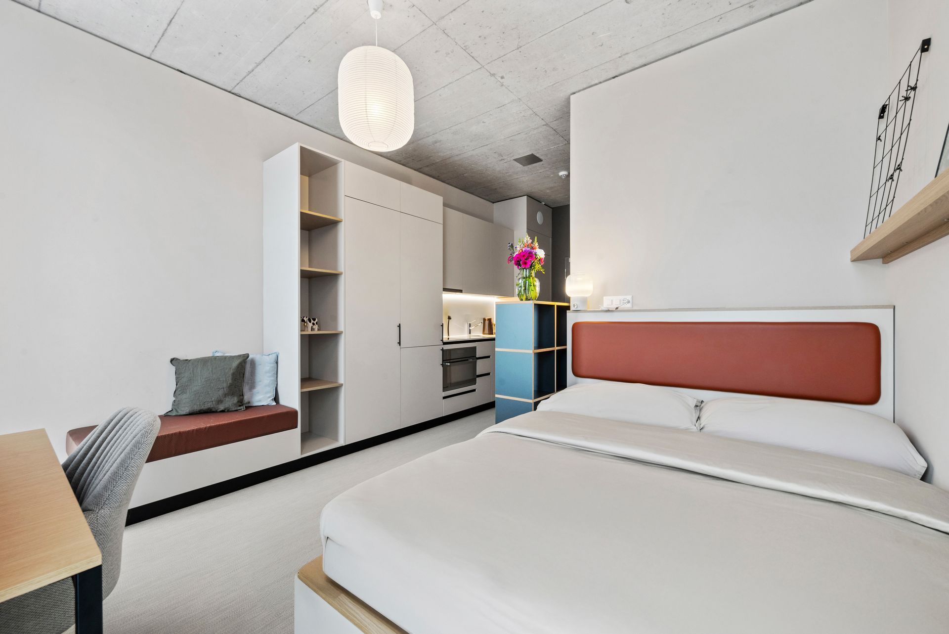 Modern bedroom with white bed, red headboard, desk, wardrobe, and blue accent cabinet