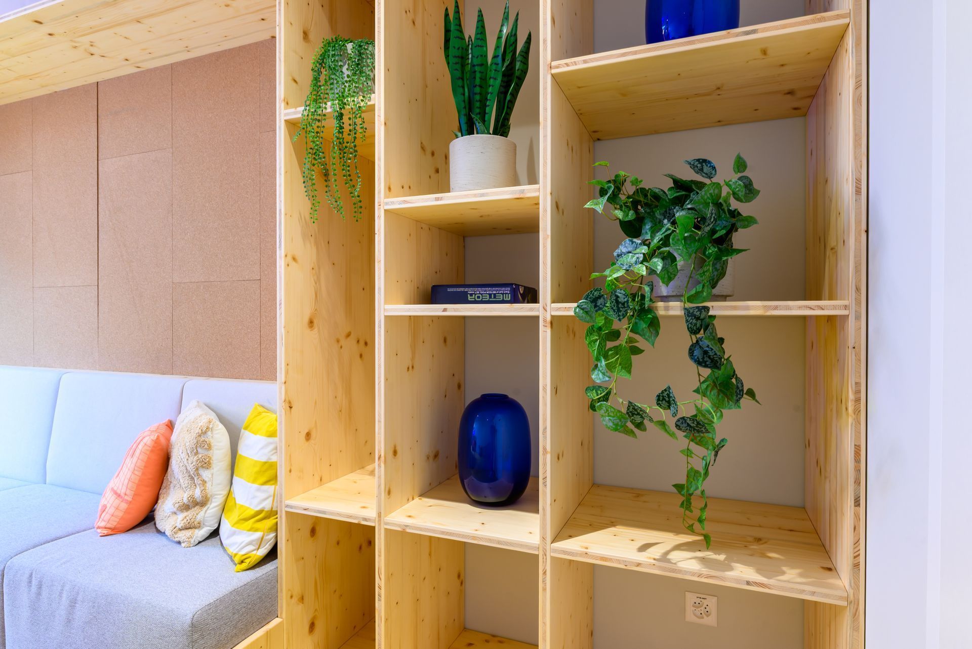 Wooden shelving with potted plants beside a light gray sofa with colorful pillows