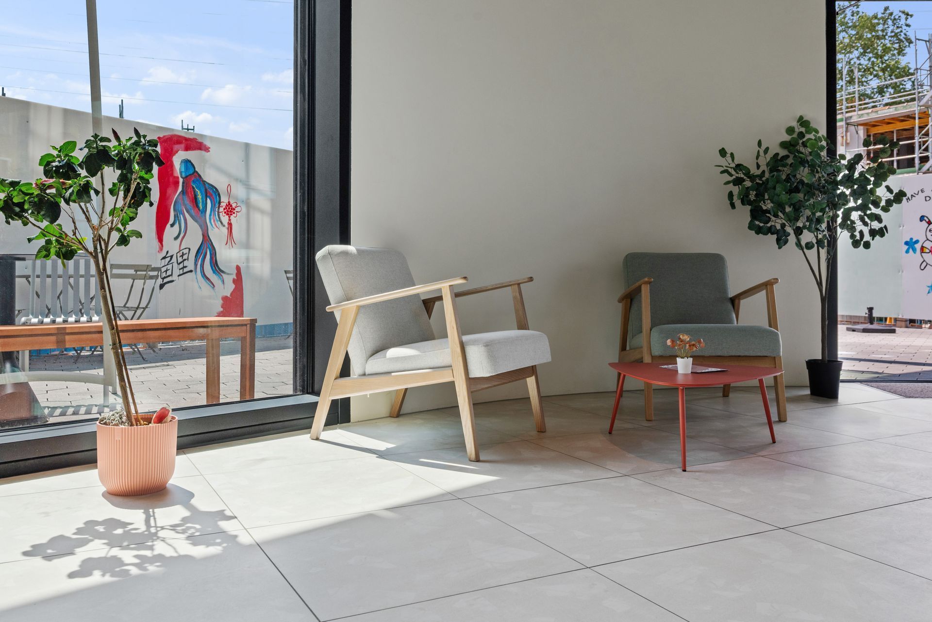 Modern patio with two chairs, small table, and potted plants on a tiled floor.