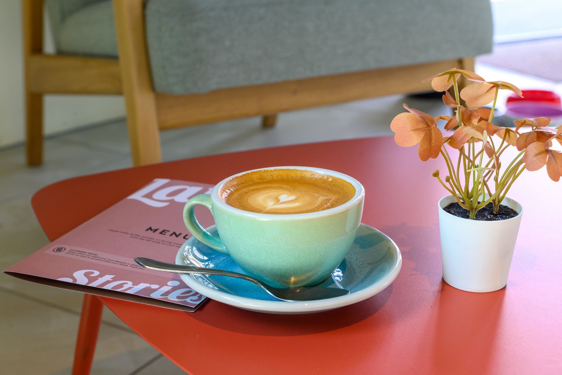 Turquoise coffee cup on a red table beside a magazine and small white vase with flowers