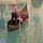Person in a small gondola on calm green water, with a striped pole and striped canopy nearby.