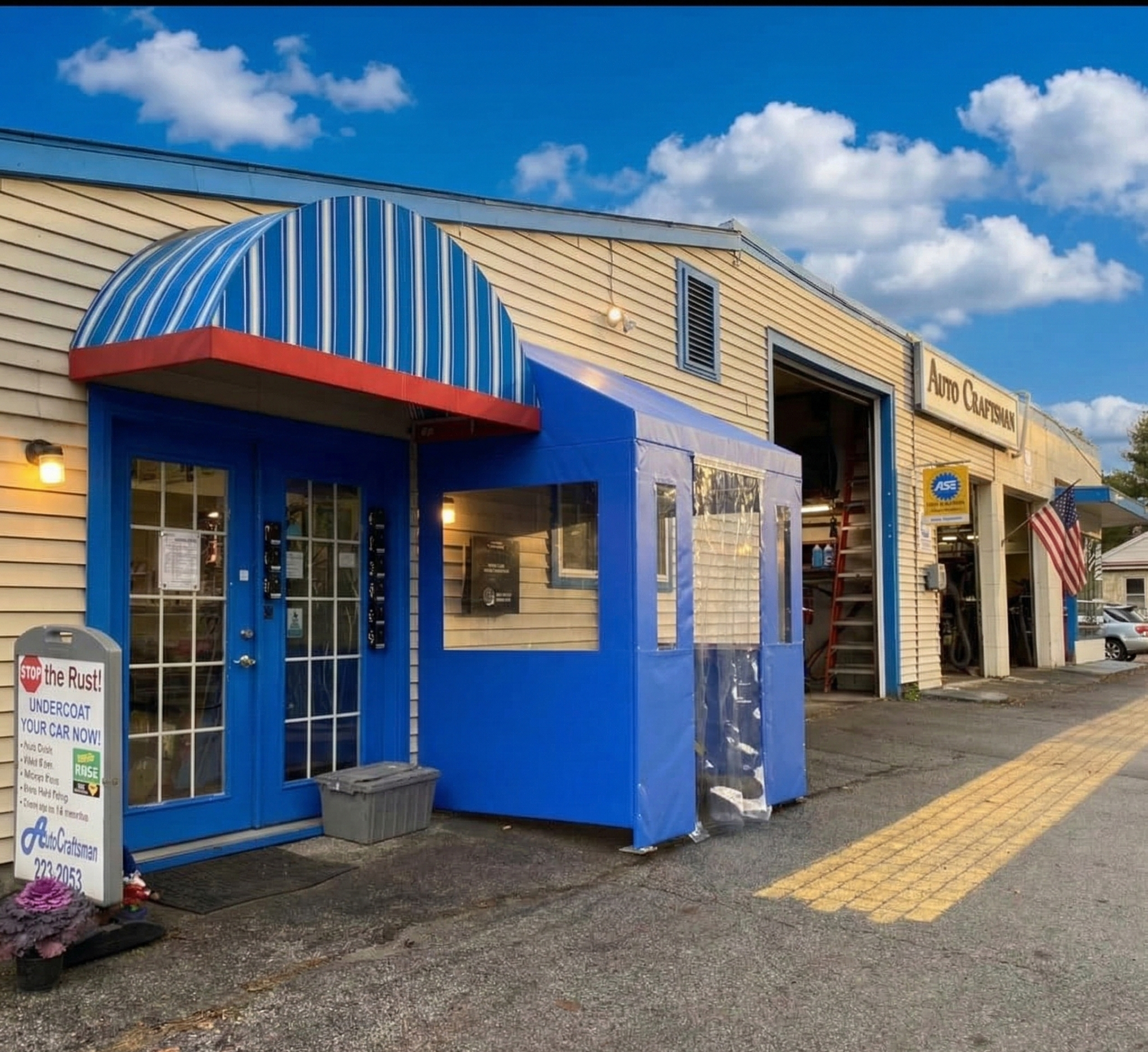 Exterior of a building featuring a blue enclosed entrance canopy, light yellow siding, and an open garage bay.