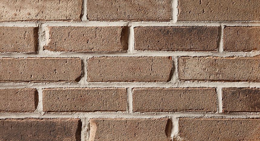 A close up of a brown brick wall with white mortar.
