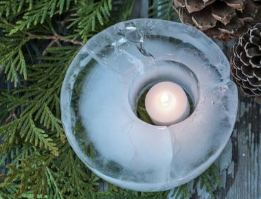 A candle in an ice ring with pine cones in the background.