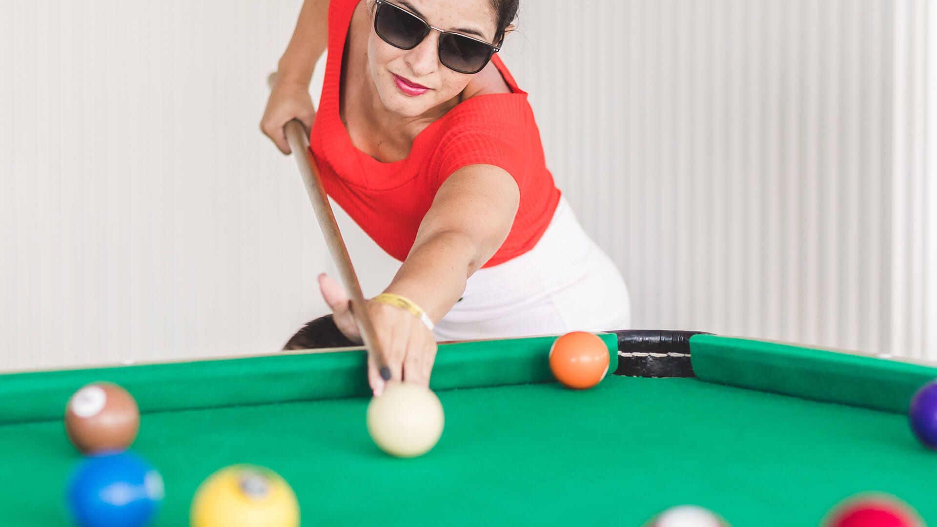Uma mulher usando óculos escuros está jogando sinuca em uma mesa de sinuca.
