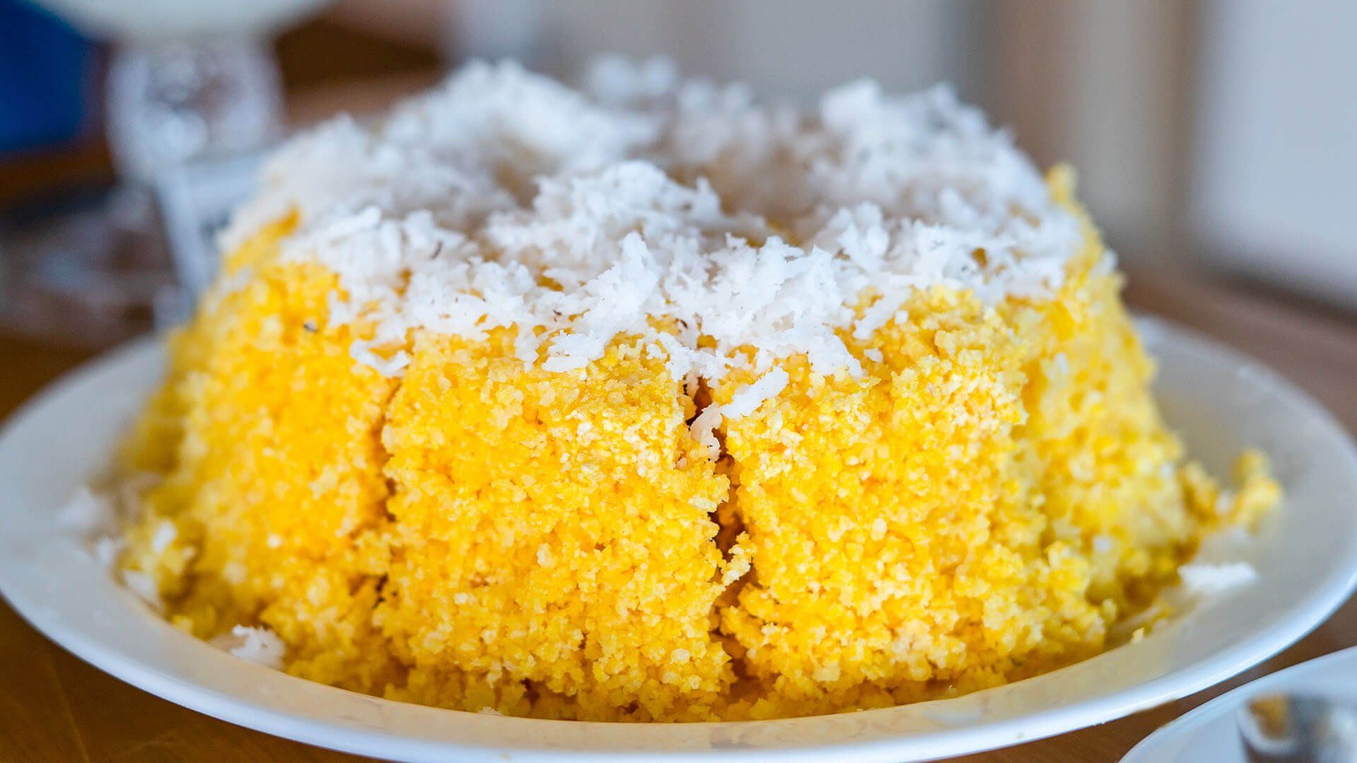 Um bolo amarelo com coco por cima está em um prato branco.